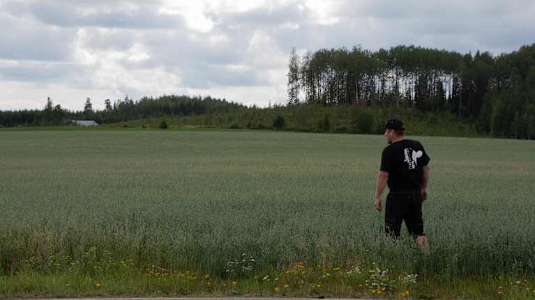 Man som går över en åker, skog i bakgrunden. 