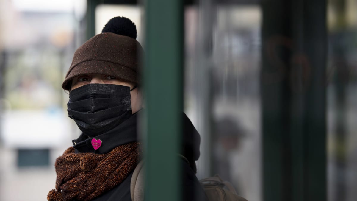 Hengityssuojaimeen pukeutunut bussipysäkillä.