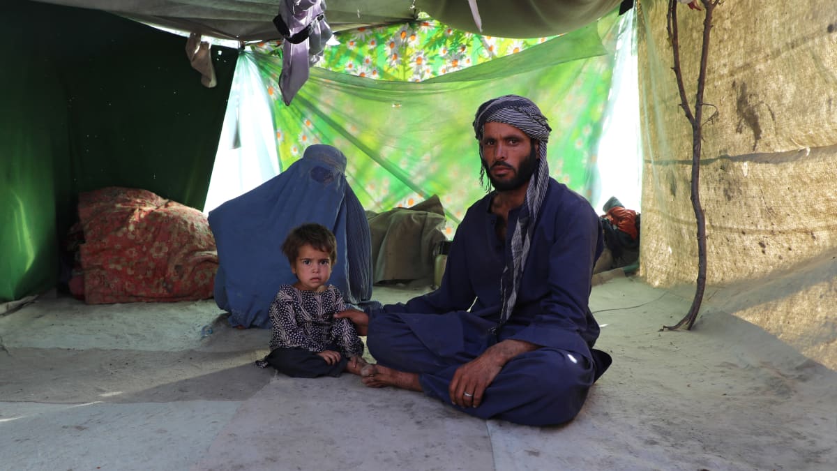 Mies, lapsi ja burkaan pukeutunut nainen istuvat teltassa pakolaisleirillä Kabulissa.
