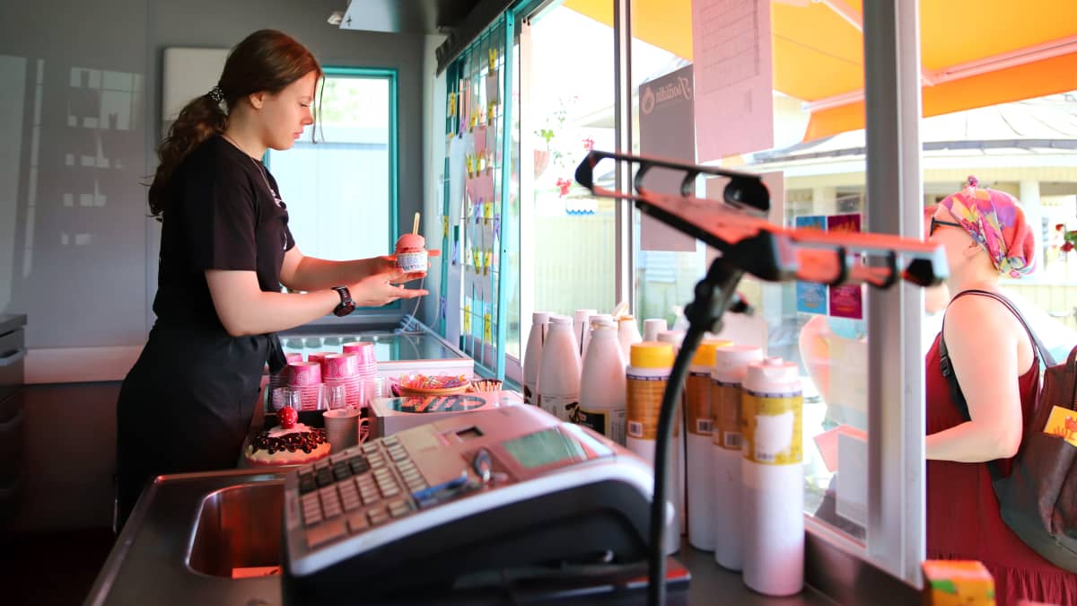 Jäätelömyyjä ojentaa jäätelöä kioskista ulkona olevalle asiakkaalle.