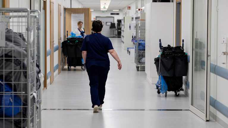 The photo shows a medical worker walking in a hospital corridor.
