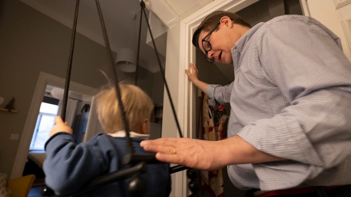 Lapsi talon sisällä olevassa keinussa, kun isä keinuttaa häntä.