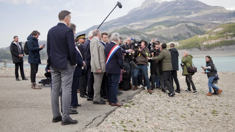 Macron tiiviin toimittajalauman ympäröimänä kuivan, surkastuneen järven rannalla.