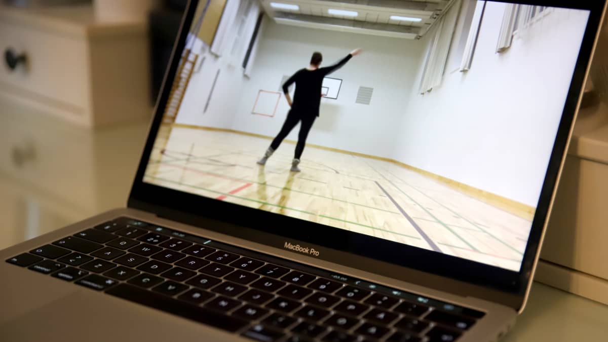 tietokoneen näytöllä video, jossa opettaja näyttää tanssikuviot tyhjässä jumppasalissa