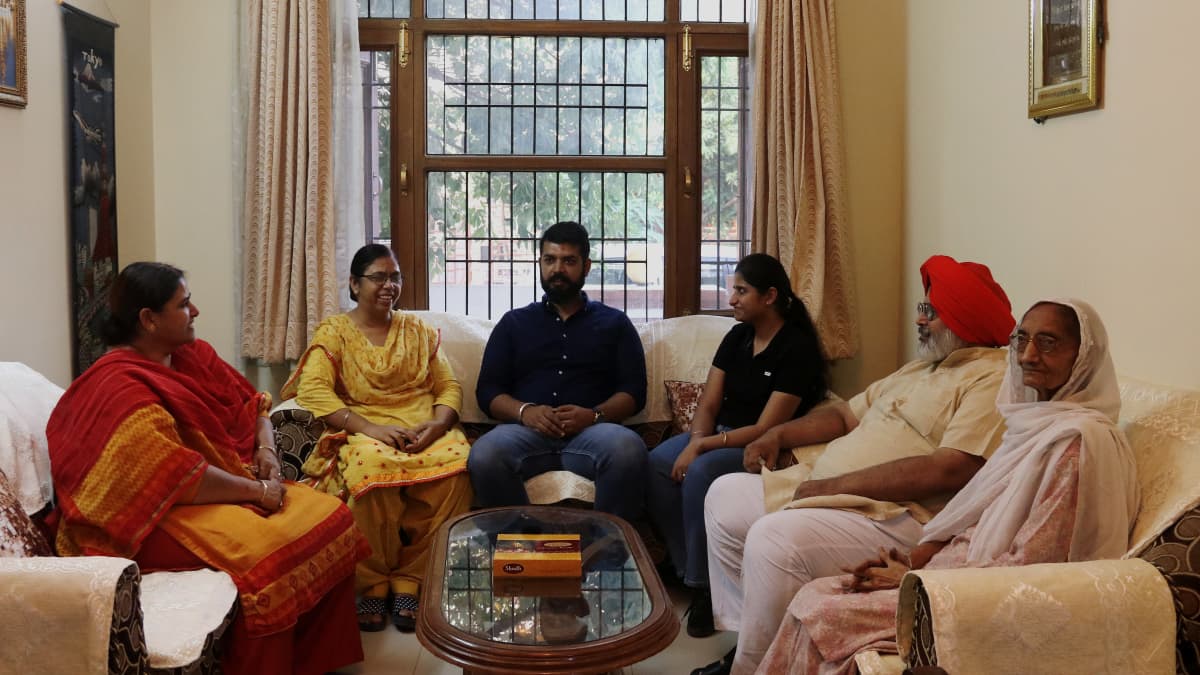 Intialainen kuusihenkinen perhe istuu sohvilla. Kuvassa on kaksi miestä ja neljä naista. Vanhemmalla miehellä on päässään punainen turbaani.