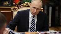 Putin selailee pöydällä olevaa lehtiötä
