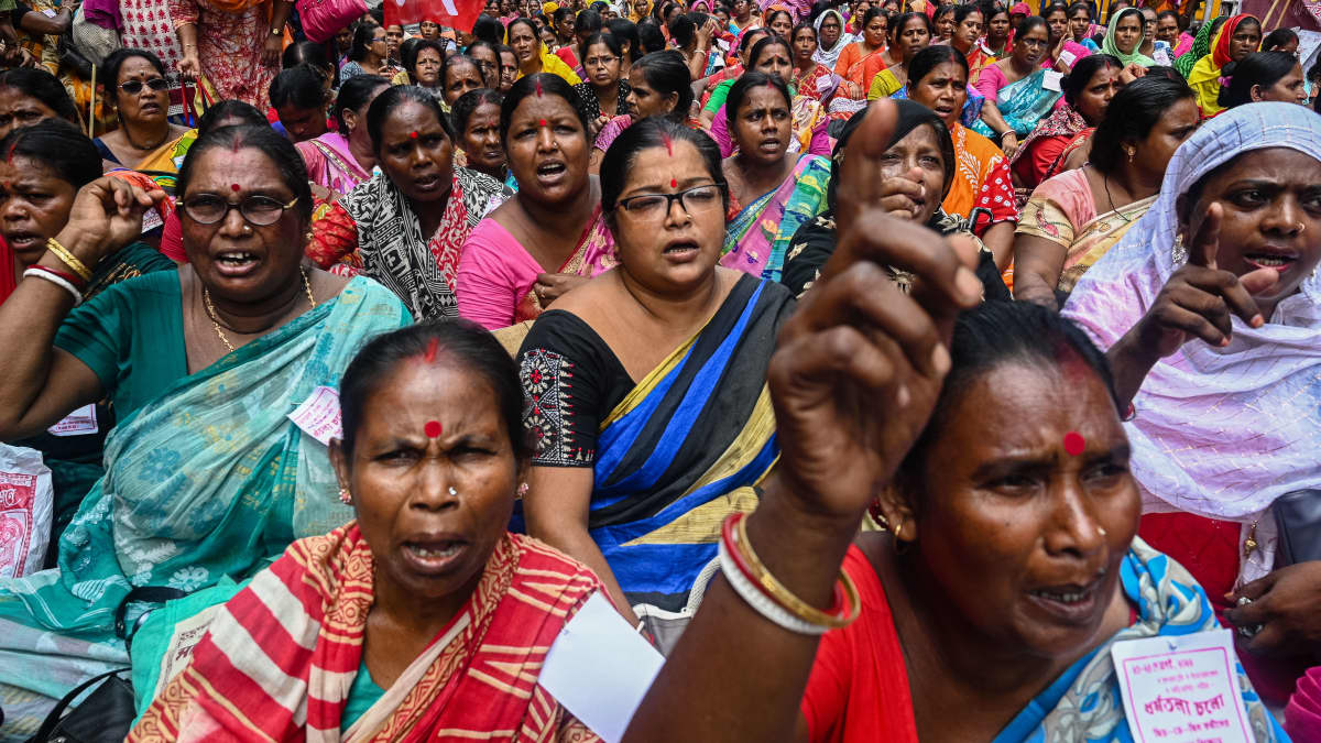 Kiukkuisia intialaisia naisia värikkäissä vaatteissa mielenosoittaa. Iso joukko ihmisiä. 