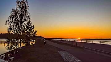 Iltahämärä laskeutuu maisemaan aikaisin keväällä, kun jäitten lähtö antaa tilaa rauhalliselle järvelle ja auringonlasku värjää taivaanrannan lämpimän oranssiksi.