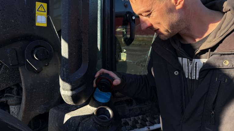 En man står och kikar ner i bränsletanken på en traktor.