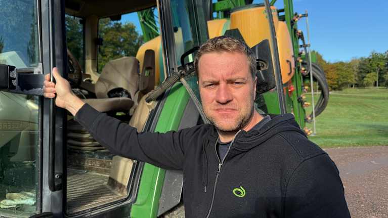 Ung jordbrukare står vid traktor.