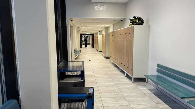 Tummiin pukeutunut oppilas kävelee koulun käytävällä. Kaapin päällä on kaksi mopokypärää.