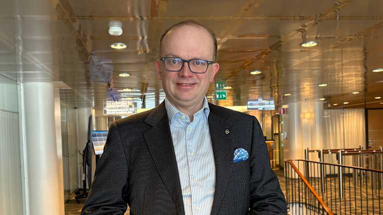 En man i kavaj och kragskjorta ler mor kameran. 