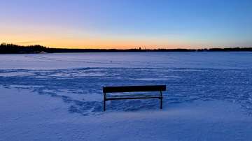Aamun värejä. Puistonpenkki jäätyneen järven rannalla selkeänä aamuna. 