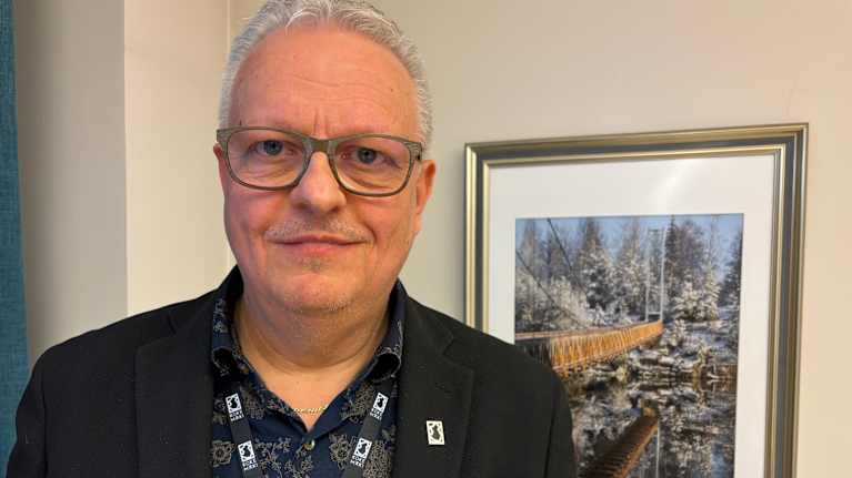 Kokemäki city manager Teemu Nieminen looks at the camera and smiles, a landscape painting can be seen in the background.