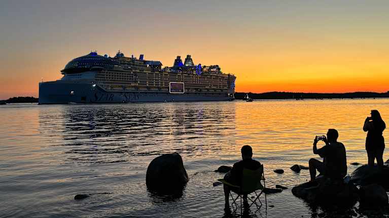 Risteilyalus "Stars of the Sea" lipuu rauhallisesti auringonlaskun aikaan Ruissalon ohi kun se lähtee Turusta. Etualalla istuu kolme ihmistä rannalla, kaksi heistä kuvaa alusta puhelimillaan.