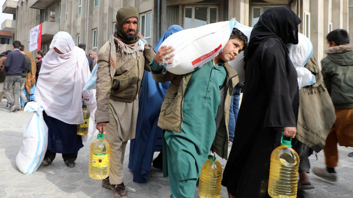 Ihmiset kantavat ruoka-apuna saamiaan öljypulloja ja jauhosäkkejä Kabulissa Afganistanissa.