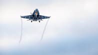 A fighter jet in the air, seen from below against a grey sky with jet trails from the tips of its wings.