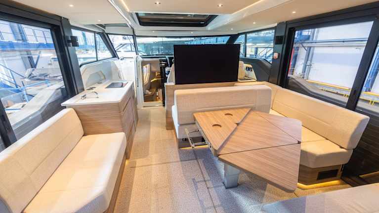 En ljus inredning i en modern båt med flera sittplatser, bord och stora fönster.