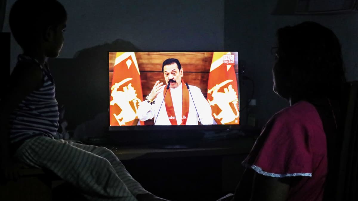 Mahinda Rajapaksa puhumassa televisiossa, televisiota katsoo vanhempi ja lapsi.