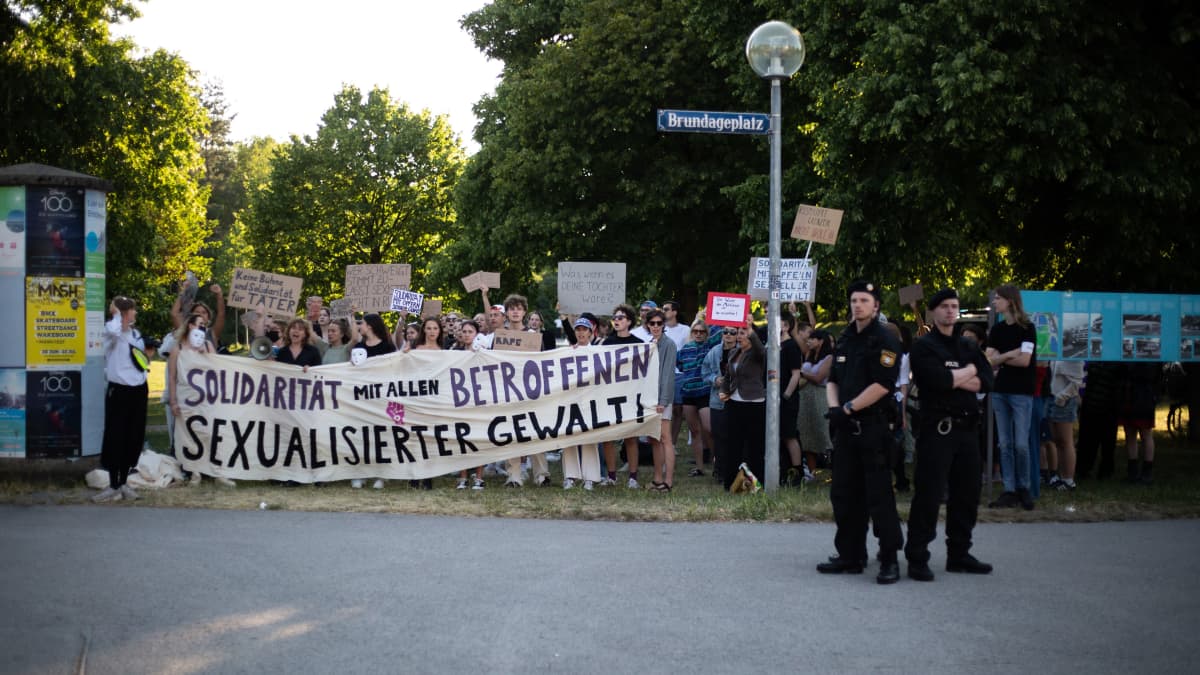 Mielenosoittajia puistossa saksankielisine banderolleineen ja kyltteineen.