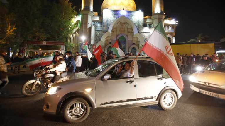 Människor i bilar och på motorcyklar bär Irans flagga och firar längs gatorna i Teheran.