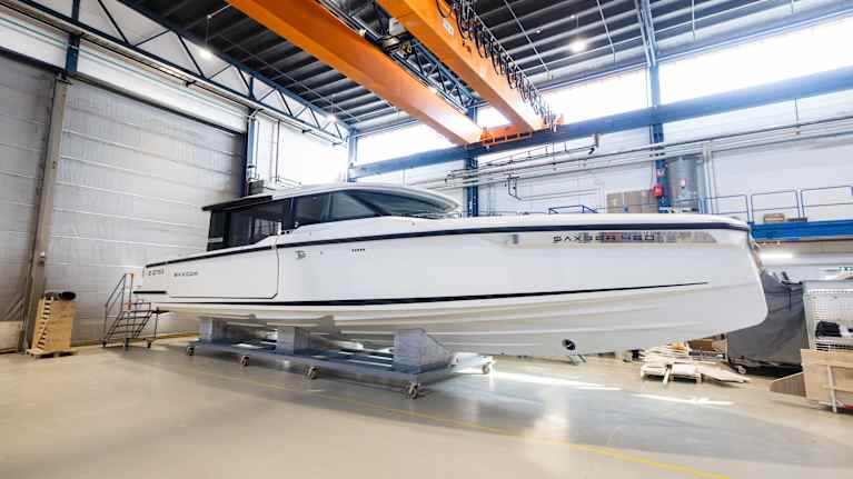 En stor vit motorbåt står uppställd inomhus i en industrilokal.