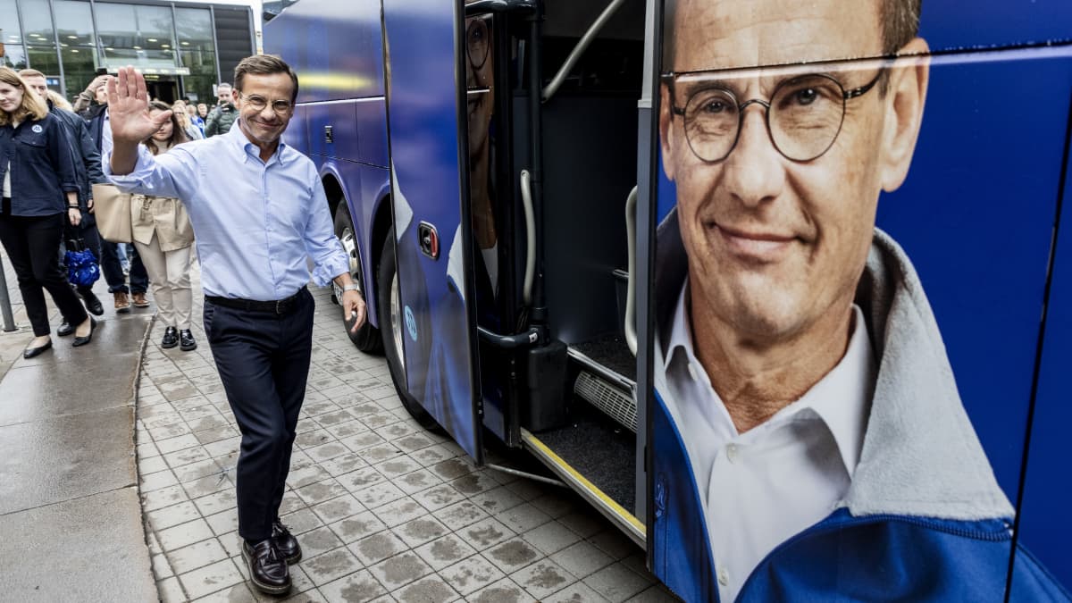 Ulf Kristersson vilkuttaa vierellään bussi, jonka kyljessä on hänen kuvansa.