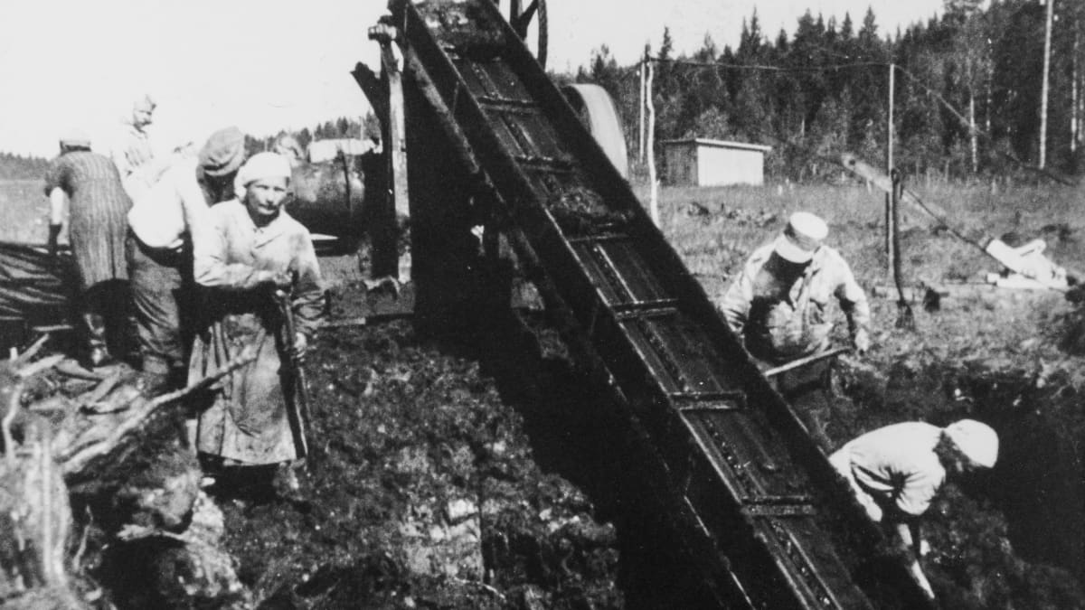 Vanhassa mustavalkokuvassa ihmiset työskentelevät jonkinlaisen koneen kanssa ulkona. 
