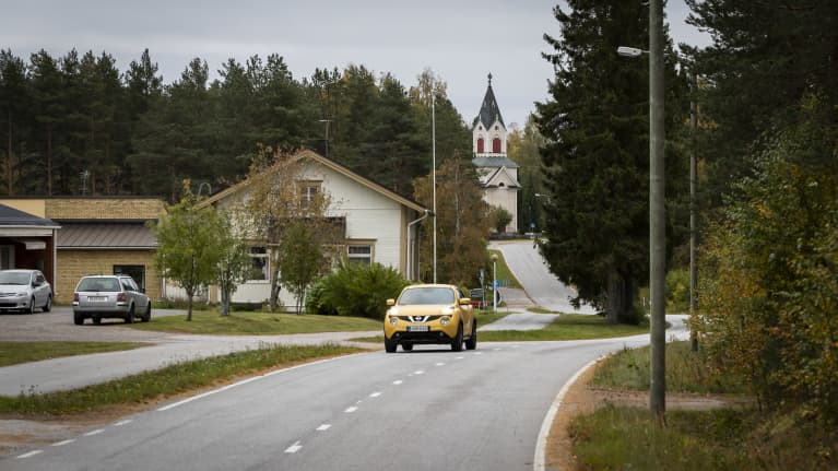 Lestijärven taajaman lävitse kulkeva tie, jolla kulkee keltainen auto. Taustalla näkyy Lestijärven kirkko. 