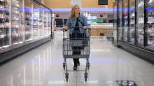 Nainen kävelee ostoskärryjen kanssa kylmäkaappien välissä.