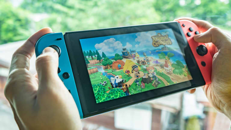 Ihmisellä on kädessään Nintendo Switch -pelikonsoli, jonka näytöllä on Animal Crossing -peli.