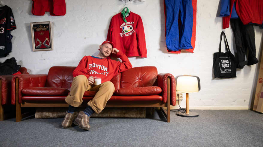 Mikko Toiviainen istuu sohvalla ja seinällä roikkuu punainen paita. 