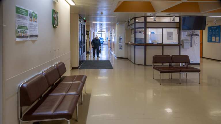 Toivakan terveysaseman aula. Tyhjiä tuoleja odotustilassa. Vanhus kävelee käytävällä.