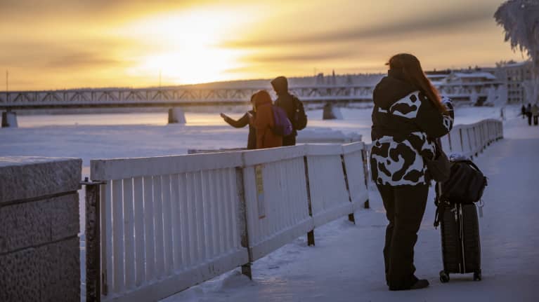 Turistit ottavat kuvia Kemijoesta Rovaniemen keskustassa auringon laskiessa.
