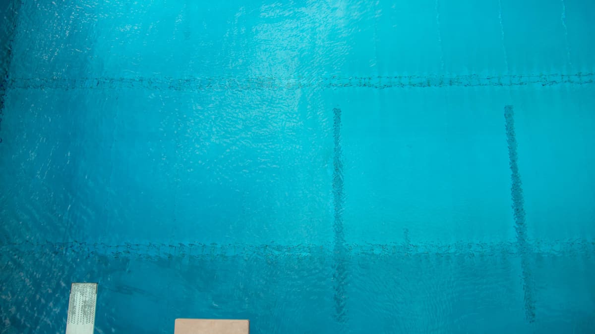 Ylhäältä hyppytornista suoraan alaspäin otettu kuva kirkkaan sinisestä uima-altaasta. Kuvan alareunassa näkyy myös hyppytasanteita.
