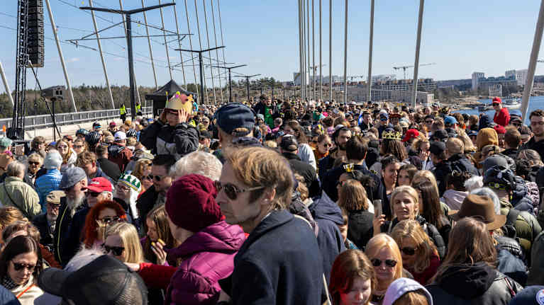 A large crowd of people gathered for the opening of the new bridge on a sunny day.