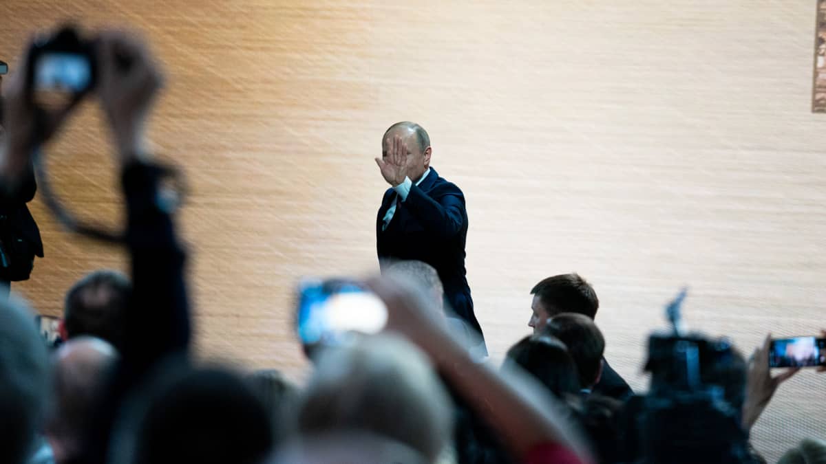 Vladimil Putin nostaa kättään ja kävelee pitkin seinän vierusta.