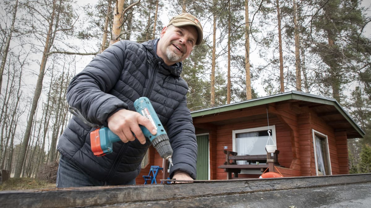 Hymyilevä Kari Kulmala korjaa puuvenettään rantasaunan luona.