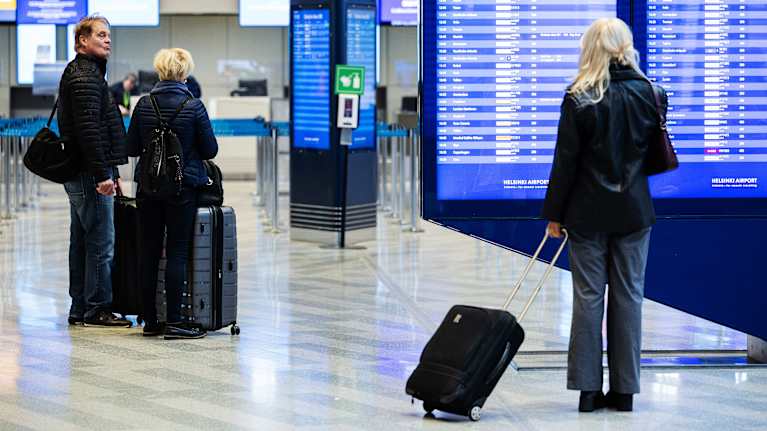 Three people with luggage and dark clothes standing in an airport terminal.
