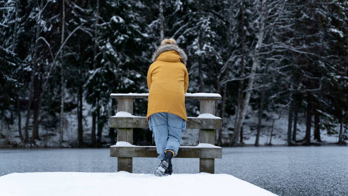 Nainen nojaa aitaa vasten järven rannalla.