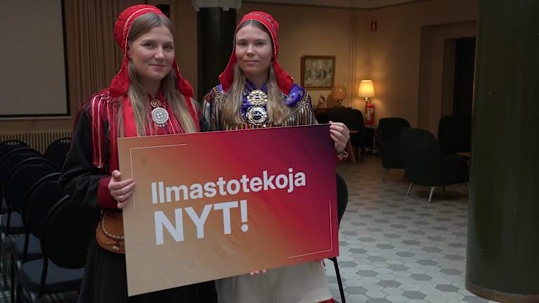 Suomen Saamelaisnuoret, Teija Kaartokallio ja Lotta Hagelin pitävät käsissään Ilmastotekoja NYT-kylttiä seisoessaan.