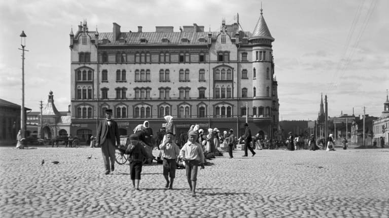 Mustavalkoinen kuva Tampereen Keskustorilta 1900-luvun vaihteessa. Kuvassa paljon ihmisiä torialueella, ja kolme pikkupoikaa kävelemässä kohti kameraa.