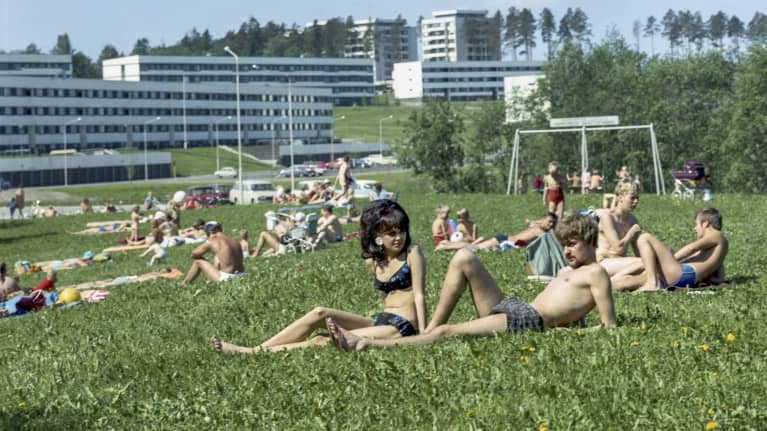 Ihmisiä ottamassa aurinkoa nurmikolla Kaukajärvellä. Kuva otettu vuonna 1969, ja sen ajan tyyli myös nähtävillä ihmisten hiuksissa ja pukeutumisessa.