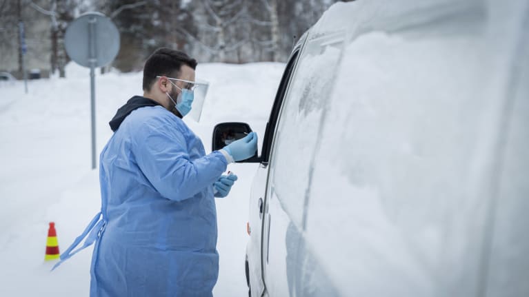 Suojavarusteisiin pukeutunut henkilö tekee koronatestiä autossa istuvalle henkilölle. 
