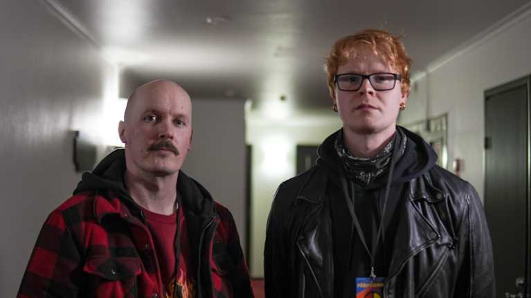 Två personer med namnskyltar står i en korridor med vita väggar.