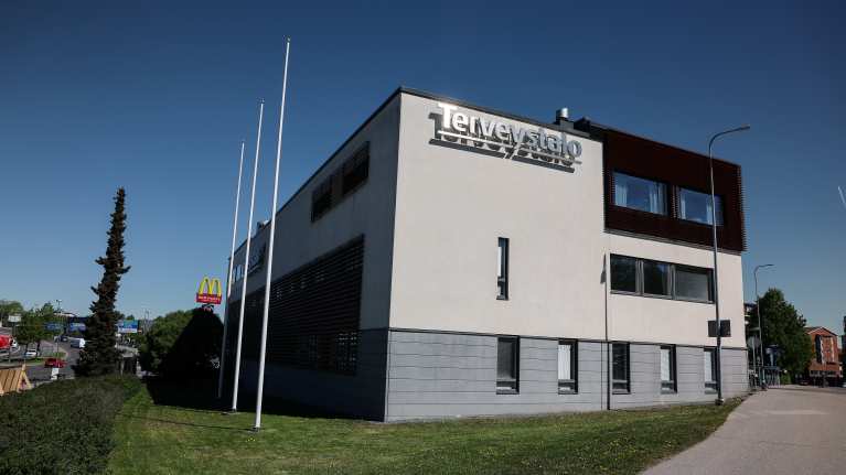 Terveystalo logo on a grey building with a blue sky in the background.