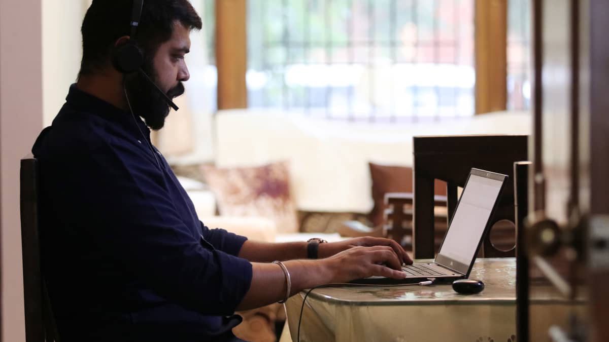 Pöydän ääressä istuva intialainen IT-asiantuntija näpyttelee läppäriä kuulokkeet päässään.