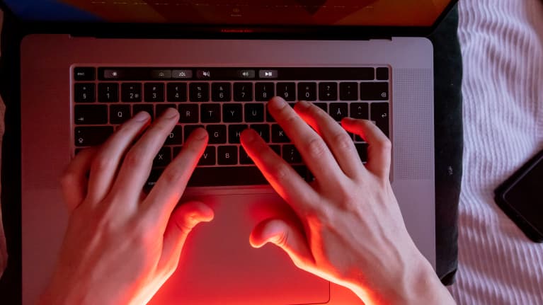 Punaisessa valossa kädet kannettavan tietokoneen näppäimistöllä.