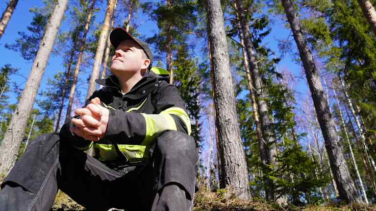 Thomas Lindholm sitter i skogen och tittar uppåt.