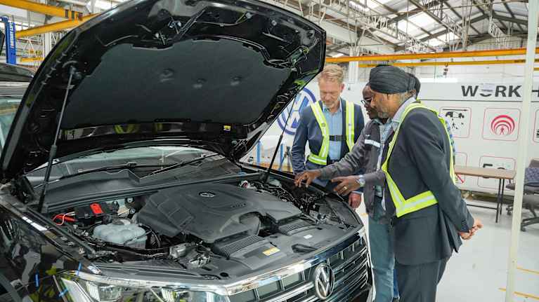 Men look under the open hood of a Volkswagen. 